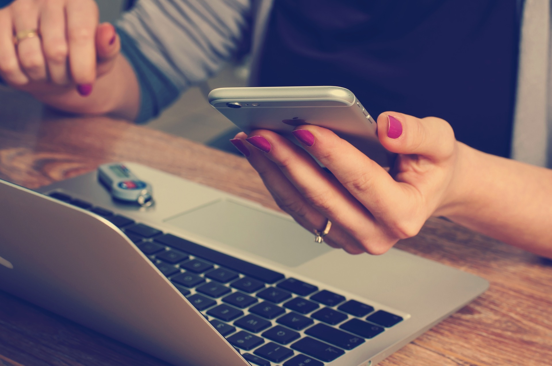 A woman looking at her smartphone while sat at her desk in front of her laptop