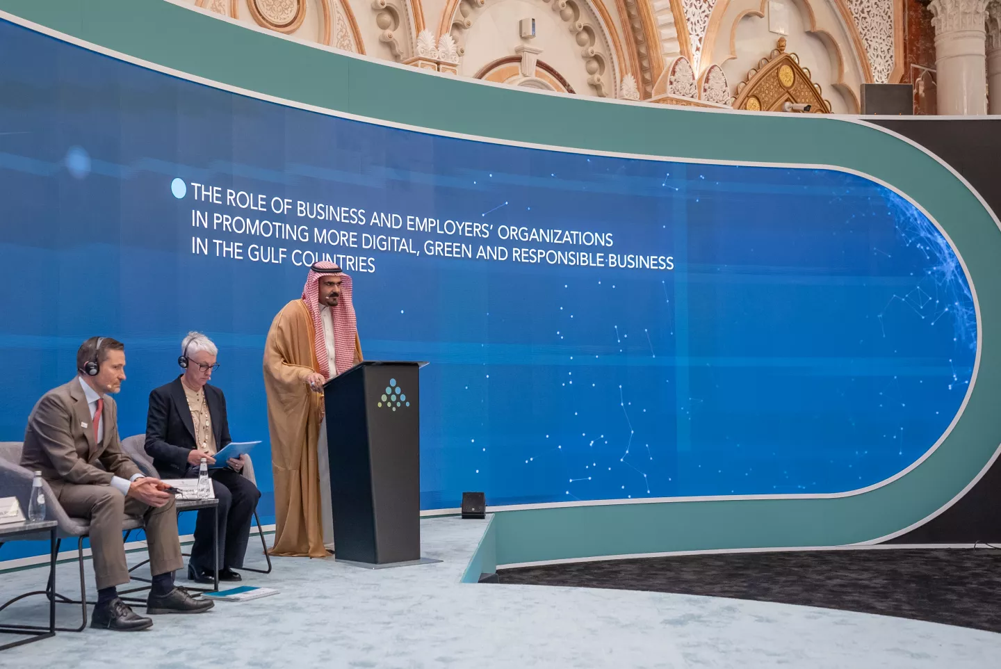 Arab man standing on a podium during an event, delivering a speech