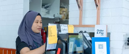 Cashier wearing a hijab processing an order at a digital payment counter